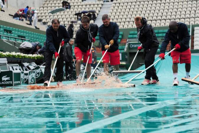 Entre les gouttes, le personnel de Roland Garros retire l'eau des bâches. 
